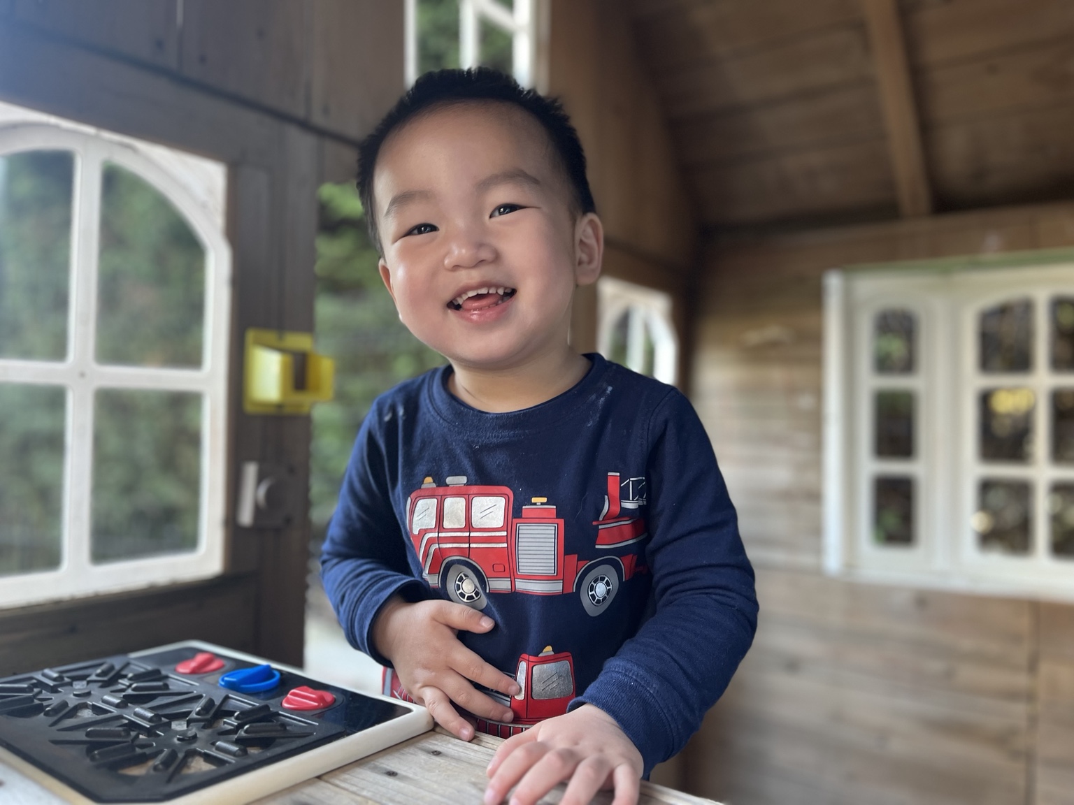 A smiling child playing inside a wooden playhouse at the daycare